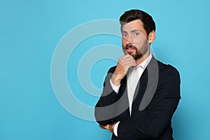 Portrait of handsome bearded man in suit on light blue background. Space for text