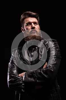 Portrait of Handsome bearded man wearing a leather jacket with serious expresion over black background