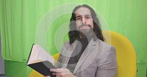 Portrait of handsome bearded Middle Eastern man sitting with book and thinking. Young man in formal suit rubbing eyes