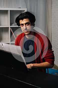 Portrait of handsome bearded young pianist man sitting at piano, looking at camera.