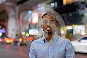 Portrait of handsome black African businessman outdoors in city at night smiling