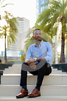 Portrait of handsome black African businessman sitting outdoors in city during summer
