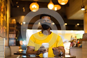 Portrait of handsome black African man wearing yellow t-shirt in coffee shop