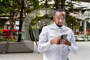 Portrait of handsome black businessman in city using phone