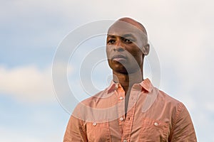 Portrait handsome black businessman glancing over the camera. Light blue cloudy sky in the background with copyspace