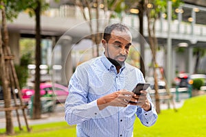 Portrait of handsome black man in city using phone