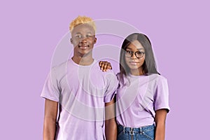 Portrait of handsome black man and his girlfriend in glasses posing and looking at camera over violet studio background