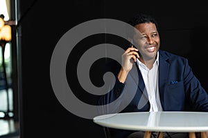 Portrait of handsome black man wearing suit and using mobile phone while sitting