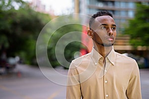 Portrait of handsome black young African businessman thinking outdoors in city