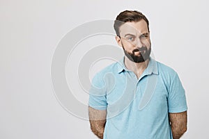 Portrait of handsome brunette with beard and moustache near white wall. His eyebrow lifted up showing his interest about