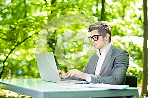 Portrait of handsome business man working at laptop at office table in green park. Business concept.