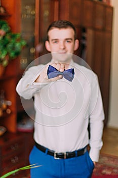 Portrait of handsome businessman in blue suit putting on bow-tie indoors