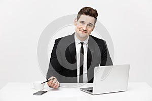 Portrait of a handsome businessman holding smartphone while working on a computer at his desk. He is in a office his