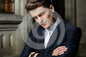 Portrait of a handsome businessman posing with crossed arms in black suit, wear watch on his hand.