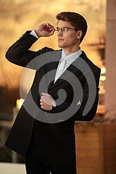 Portrait of a handsome businessman posing in eyeglasses and black suit, wear watch on his hand.