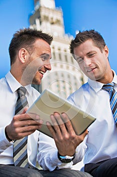 Portrait of handsome businessman showing business plan to the other businessman over digital tablet while sitting