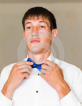 Portrait of handsome businessman in suit putting on bow-tie indoors