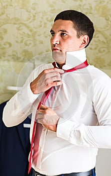 Portrait of handsome businessman in suit putting on necktie indoors