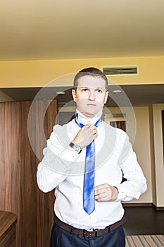 Portrait of handsome businessman in suit putting on necktie indoors