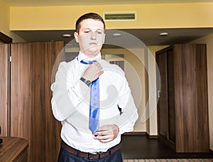 Portrait of handsome businessman in suit putting on necktie indoors