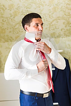 Portrait of handsome businessman in suit putting on necktie indoors