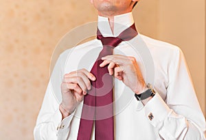 Portrait of handsome businessman in suit putting on necktie indoors close-up