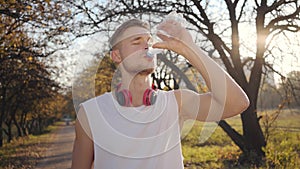 Portrait of handsome Caucasian athletic boy drinking water in sunlight and smiling. Young sportive boy training outdoors