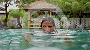 Portrait of handsome caucasian man, with Long Black Hair, Swimming in blue water of pool outside, Slowmo, close-up