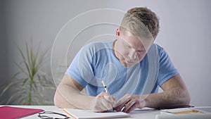 Portrait of handsome caucasian man sitting at the table and writing. Intelligent young businessman thinking and taking
