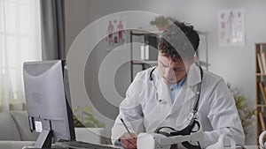 Portrait of Handsome Caucasian Medical Doctor Wearing White Coat and Stethoscope Crosses Arms, Sitting in His Health