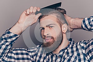 Portrait of handsome cheerful bearded young man combing his hair