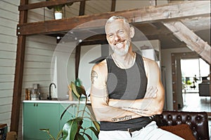 Portrait of a handsome cheerful caucasian mature man keeping arms crossed, smiling at camera while standing at his