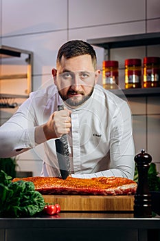 Portrait of handsome chef cooking raw meat in the kitchen. ÃÂ¡hef holds a professional kitchen knife. Concept of Cooking process