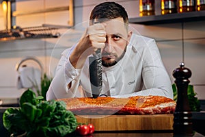 Portrait of handsome chef cooking raw meat in the kitchen. Ð¡hef holds a professional kitchen knife. Concept of Cooking process