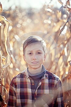 Portrait of handsome child boy among leaves corn in warm autumn day. Smile kid walking in fall park