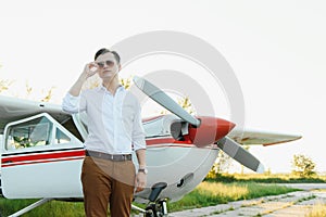 Portrait of handsome commercial pilot in captain white uniform standing and looking smart near small private helicopter on a