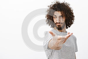 Portrait of handsome confident macho man with beard and curly hair, pulling hand towards camera as if intoducing