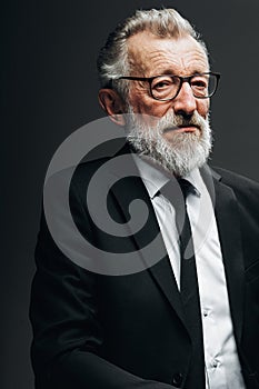 Portrait of handsome elderly CEO posing in black formal suit on dark background