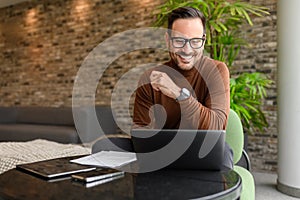 Portrait of handsome engineer working on project over laptop while sitting at table in modern office