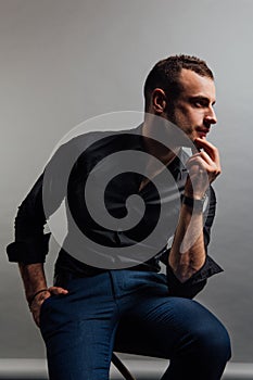 Portrait handsome fashionable man in a black shirt sits on a chair in a photo studio loft.