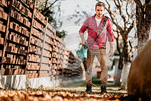 Portrait of handsome gardener using garden blower and vacuum. Home gardening details