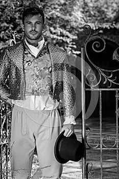 Portrait of handsome gentleman dressed in vintage costume, holding top hat in stately home courtyard