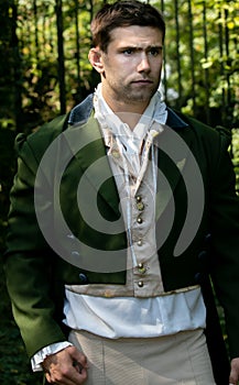 Portrait of handsome gentleman dressed in vintage costume standing in stately home courtyard with railings in background