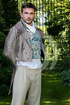 Portrait of handsome gentleman dressed in vintage costume standing in stately home courtyard with railings in background