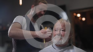 portrait of handsome gray-haired elderly man with beard cut by hair master, a professional barber streaks gray hair to