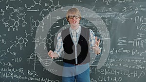 Portrait of handsome guy maths teacher talking looking at camera near chalkboard