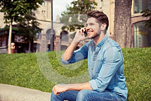 Portrait of a handsome guy sitting on parapet and talking on phone