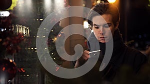 Portrait of handsome guy using smartphone on a busy city street in evening