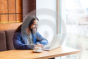 Portrait of handsome happy bearded young adult man freelancer in casual style sitting in cafe and chating with his friend in