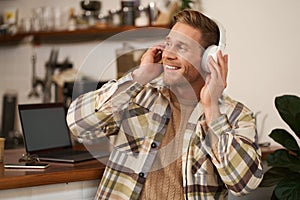 Portrait of handsome happy guy, freelancer working and listening to music in wireless headphones, dancing on his chair